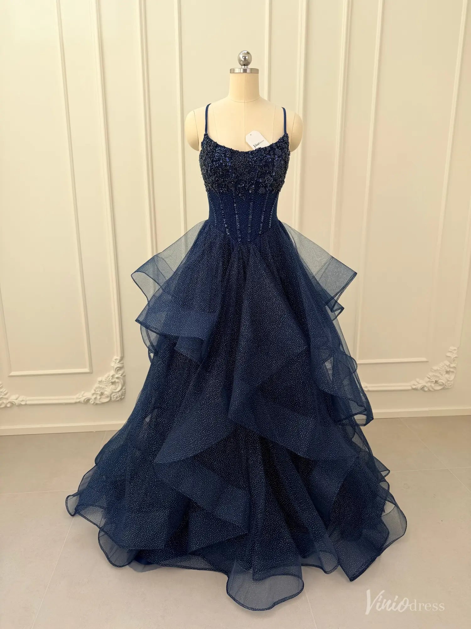 Navy blue glitter tulle ball gown with a beaded corset bodice and dramatic tiered ruffle skirt on a mannequin.