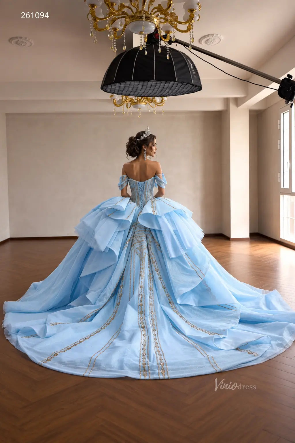 Light blue off-shoulder quinceañera ball gown with gold-beaded vertical patterns, sculptural tiered peplum, and corset back.
