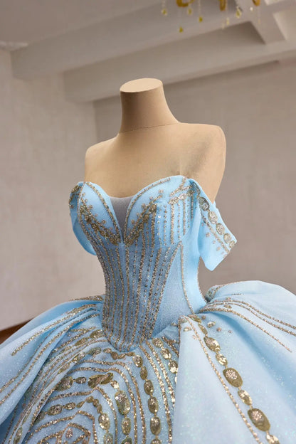 Light blue quinceañera ball gown with gold-beaded corset, off-shoulder sleeves, and sculptural tiered peplum waist.