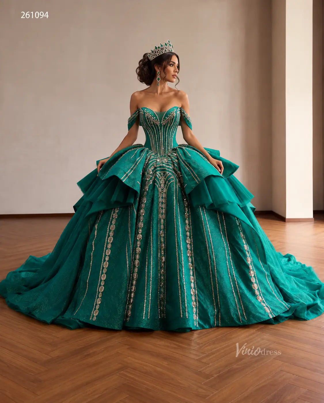 Emerald green quinceañera ball gown with gold-beaded corset, sculptural tiered peplum, and off-shoulder sweetheart neckline.