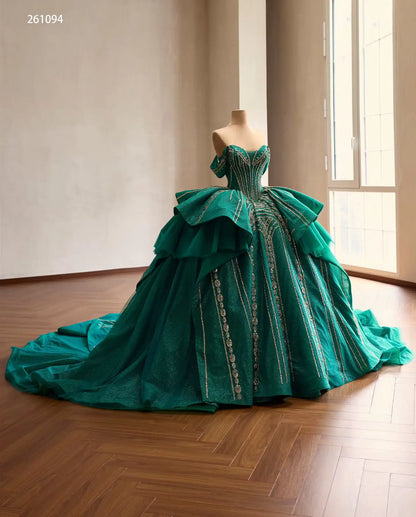 Emerald green off-shoulder quinceañera ball gown with gold-beaded corset, tiered peplum, and a sweeping glitter skirt.