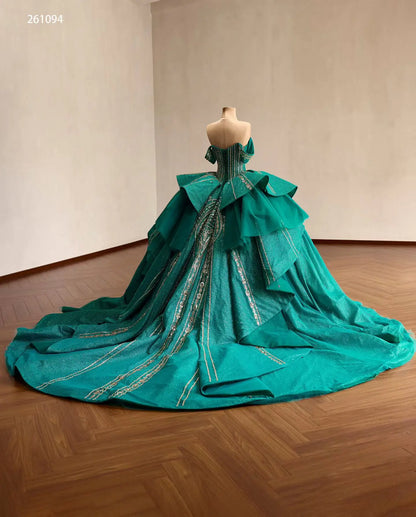 Emerald green quinceañera ball gown with gold-beaded corset, sculptural tiered peplum, and a sweeping train.