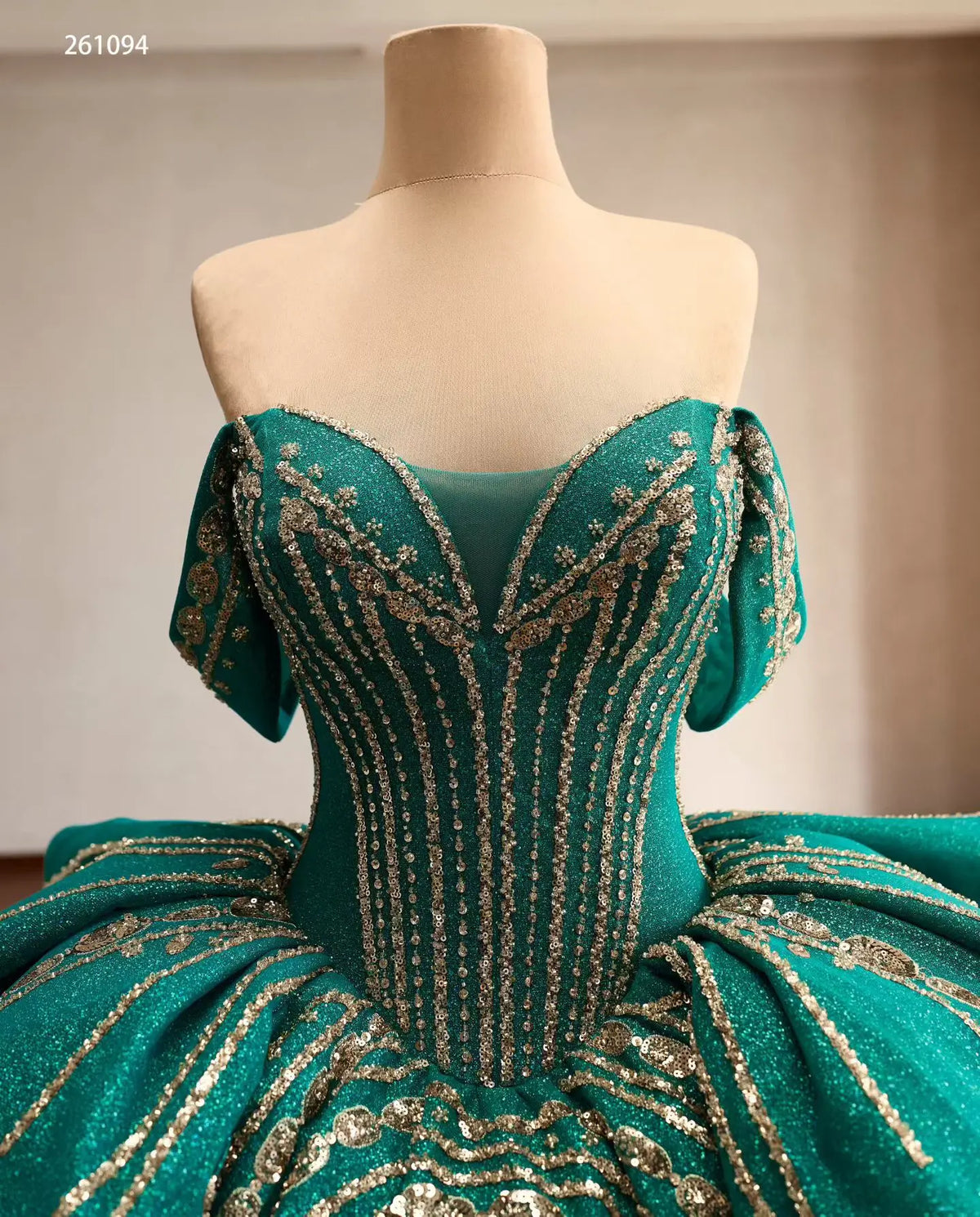 Emerald green quinceañera ball gown with gold-beaded corset, off-shoulder sleeves, and sculptural tiered peplum waist.