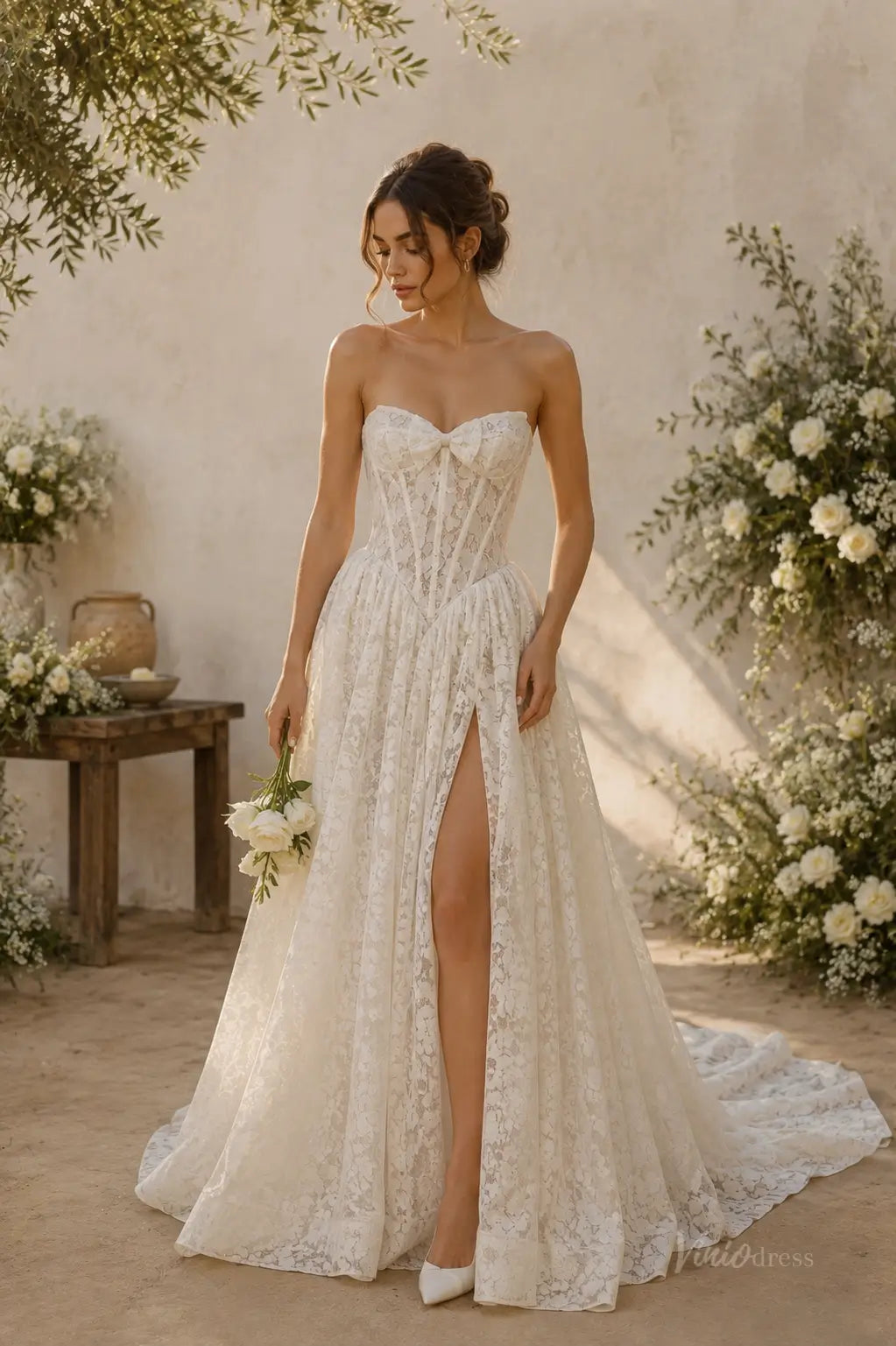 Strapless white lace wedding dress with a corset bodice, sweetheart neckline, and a high leg slit in a rustic setting.