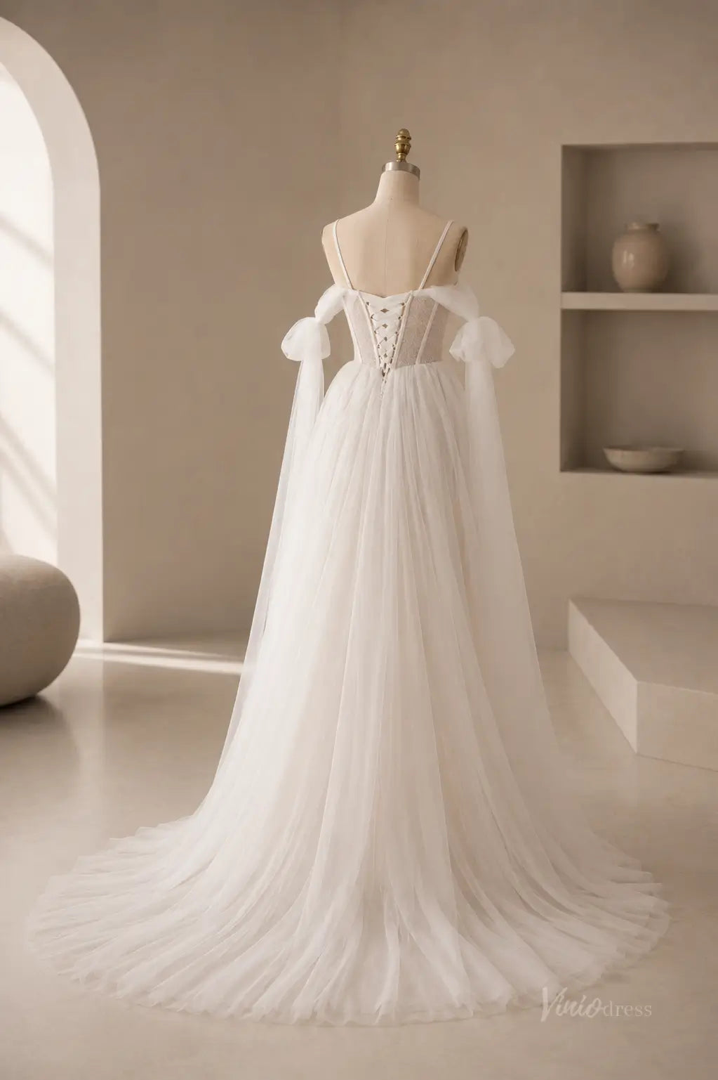 White A-line wedding dress with a corset back, spaghetti straps, and sheer off-the-shoulder tulle sleeves on a mannequin.