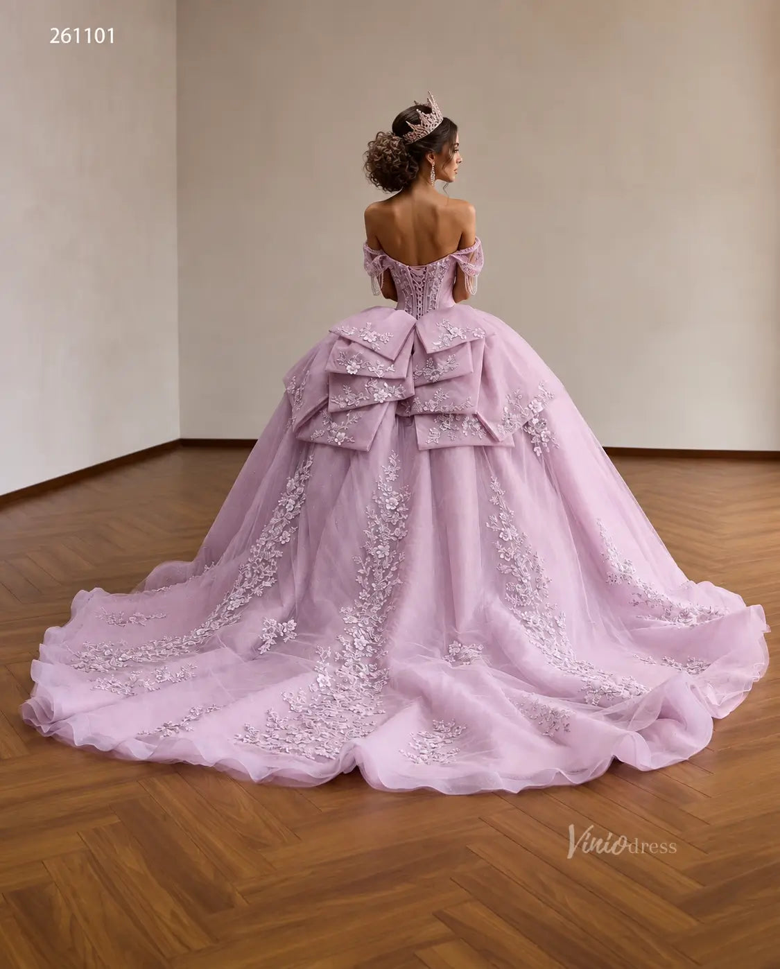 Lilac quinceañera ball gown with a crystal corset, 3D floral appliqués, off-shoulder straps, and a layered back bow.