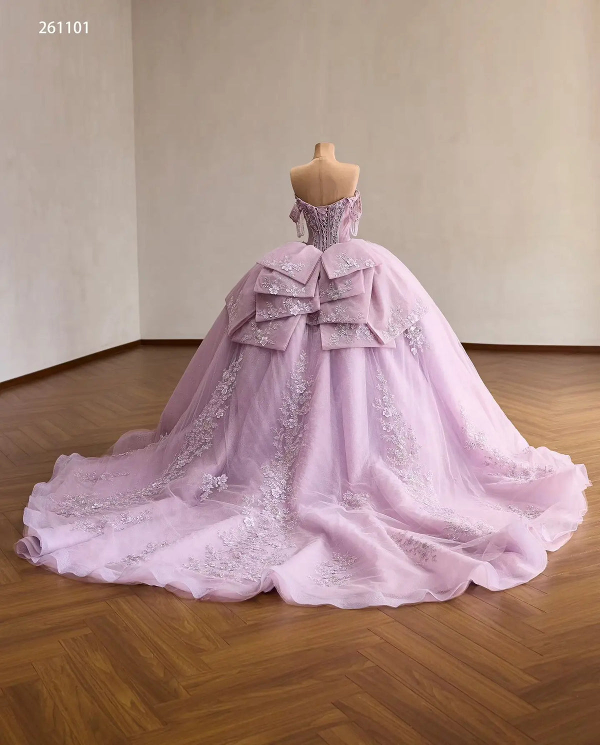 Lilac quinceañera ball gown with crystal corset, 3D floral appliqués, off-shoulder drapes, and a large layered back bow.