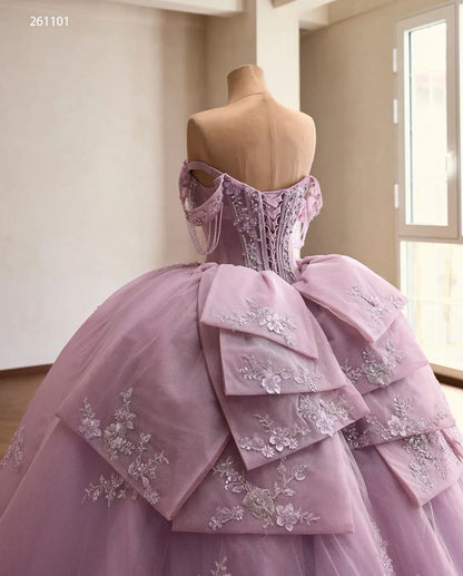 Lilac quinceañera ball gown with a crystal corset, off-shoulder beaded drapes, and a layered floral lace back bow.