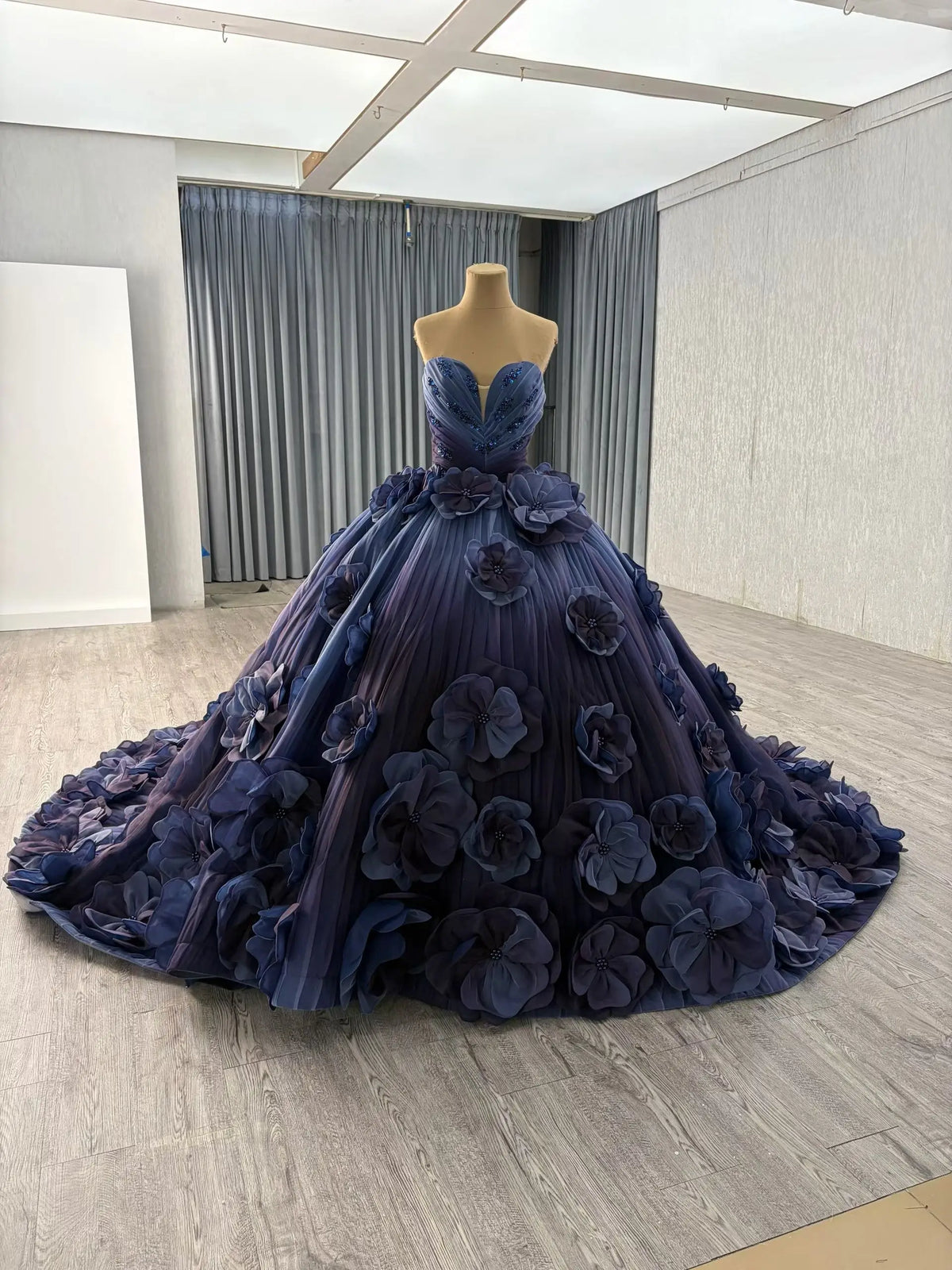 Luxury navy blue ball gown with a sweetheart neckline, 3D floral petal appliqués, and a dramatic floor-length train.