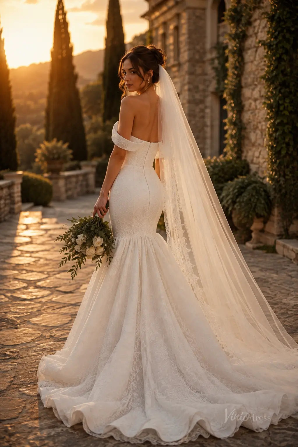 Off-the-shoulder white lace mermaid wedding dress with a long veil and train, set against a sunset garden backdrop.