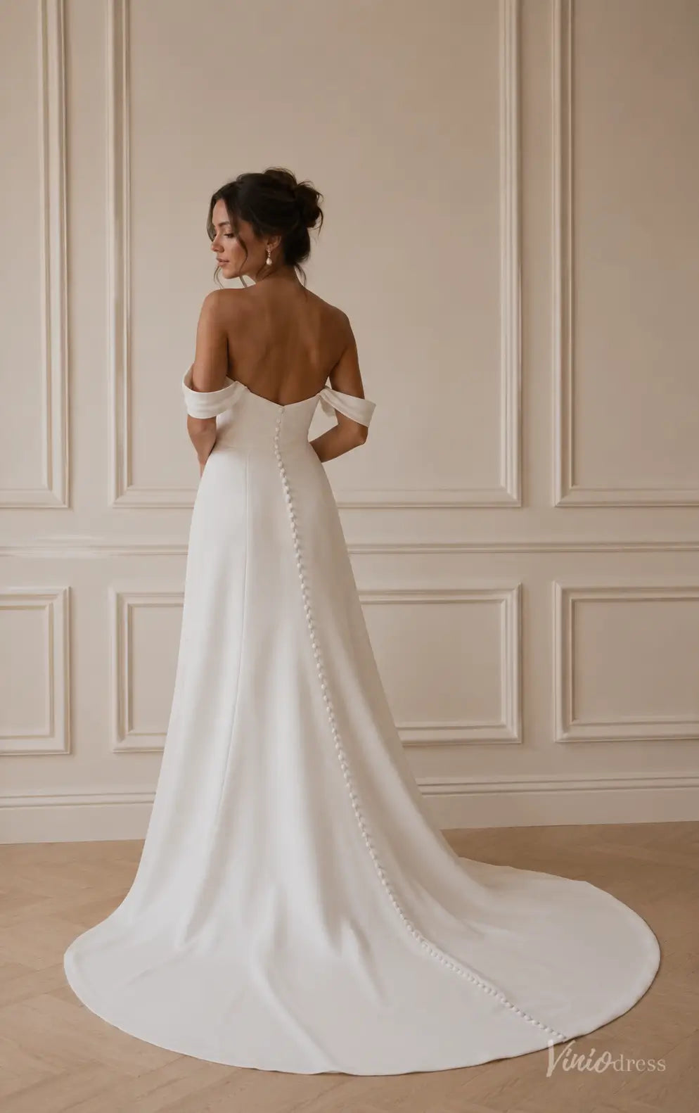 Minimalist white satin off-shoulder wedding dress with a button-back bodice and flowing chapel train.
