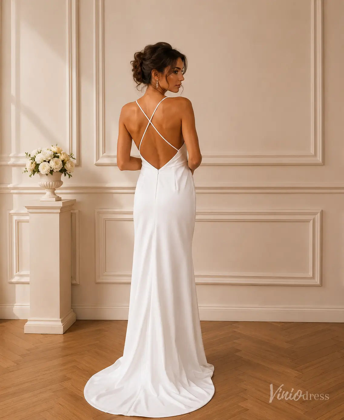 Minimalist white satin wedding dress with an open crisscross back, spaghetti straps, and a flowing floor-length skirt.