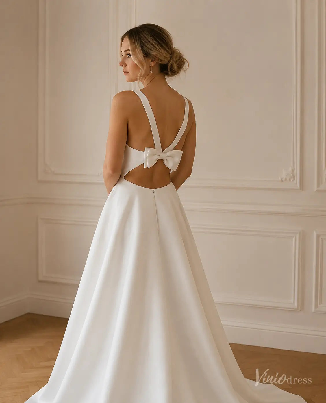 Minimalist white satin A-line wedding dress with a V-neck, open back, and statement bow detail.