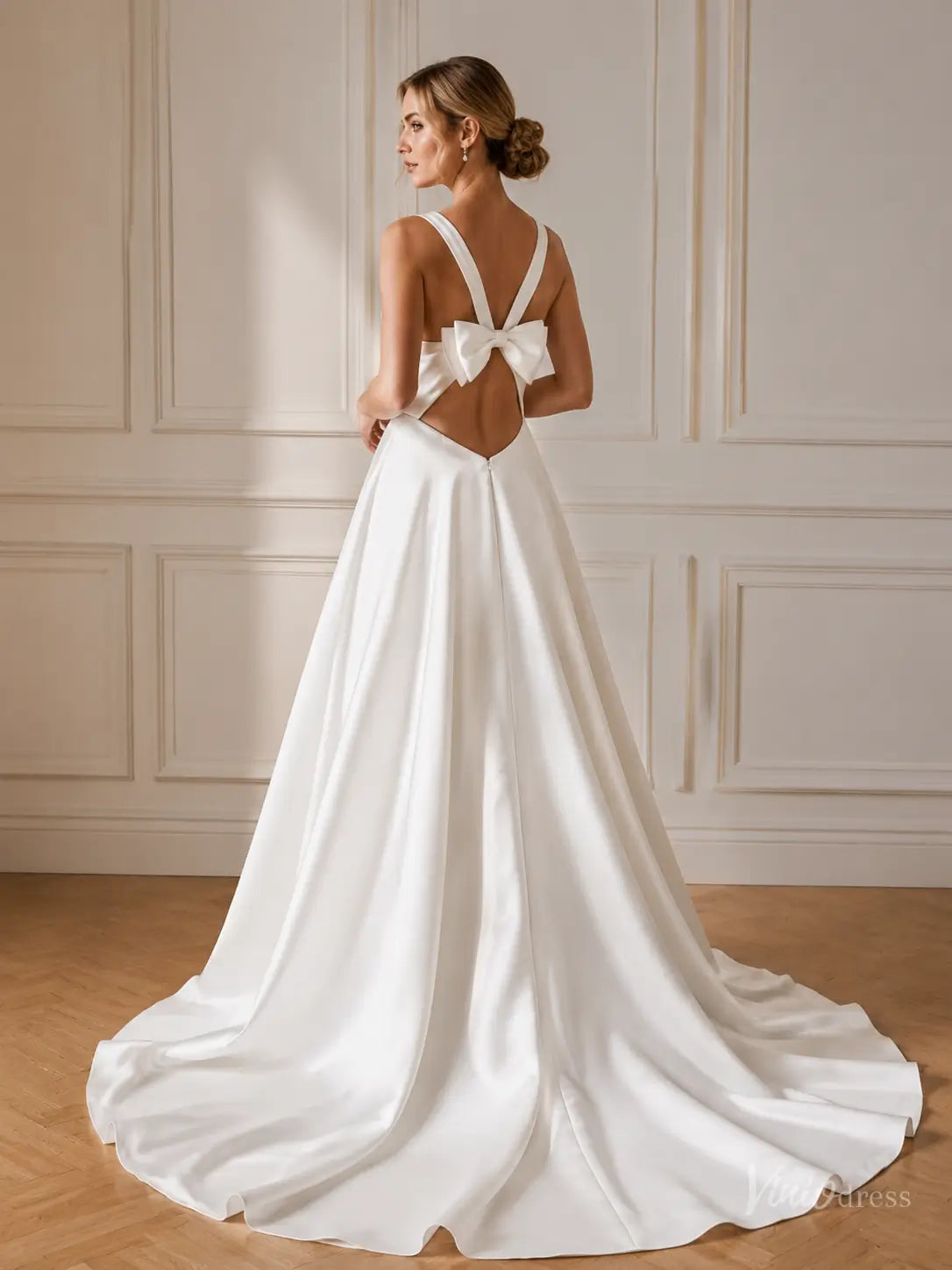 Minimalist white satin A-line wedding dress with an open back, statement bow detail, and flowing floor-length skirt.