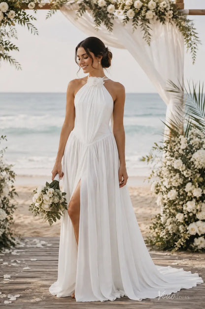 White A-line chiffon beach wedding dress with a halter neckline, floral detail, and a high side slit on a sandy shore.