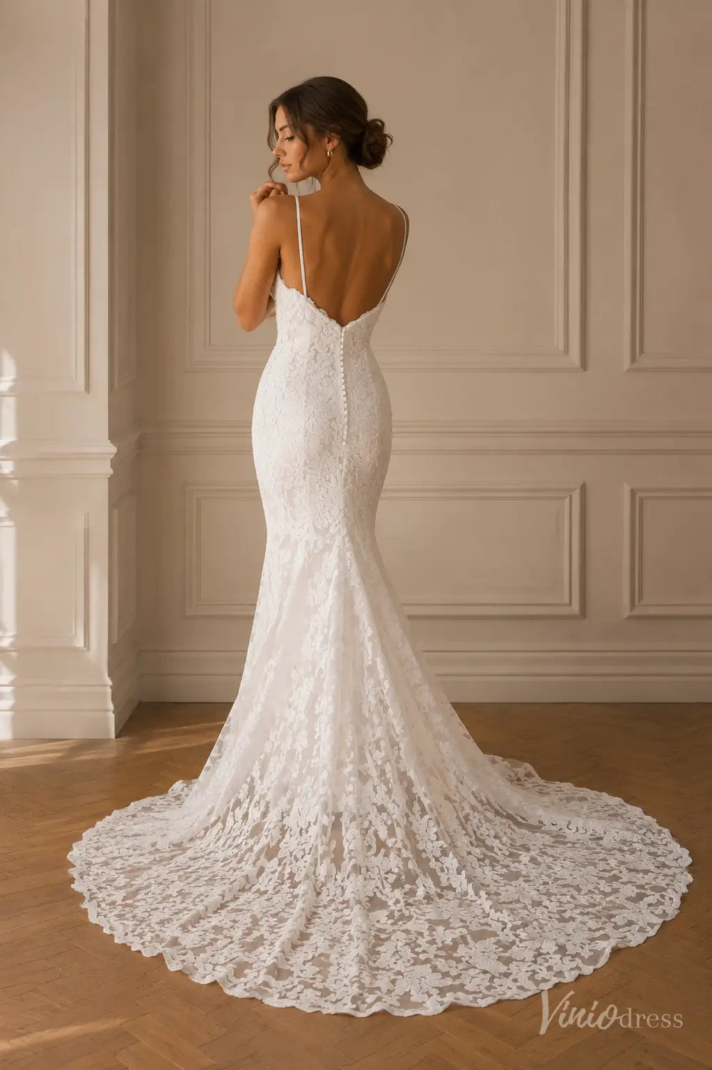 White lace mermaid wedding dress with spaghetti straps, a low back, and a long train with button-up detailing.