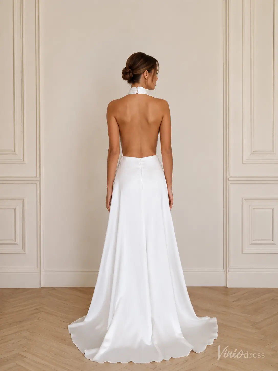 Minimalist white satin wedding dress with a halter neckline, open back, and flowing A-line skirt.