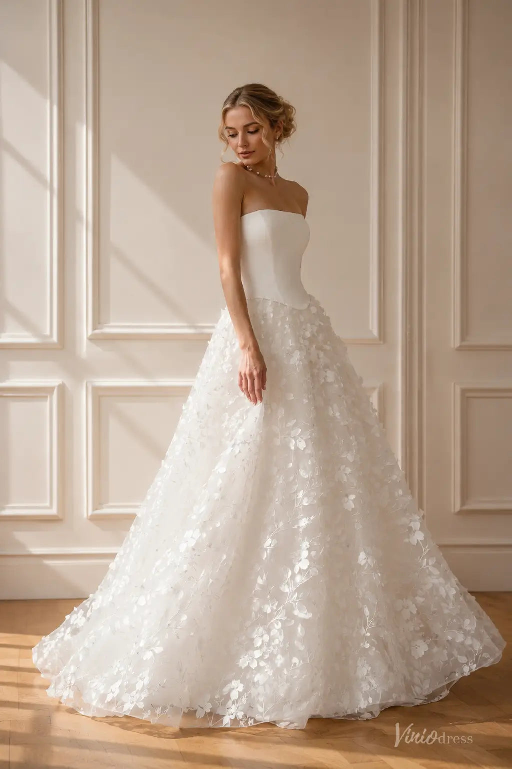 Strapless white wedding dress with a sleek bodice and a full skirt featuring delicate floral lace appliqués.
