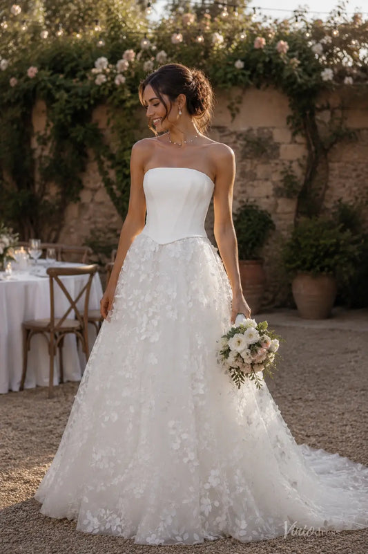 Strapless white wedding dress with a structured bodice and a floral applique A-line skirt, held by a bride outdoors.