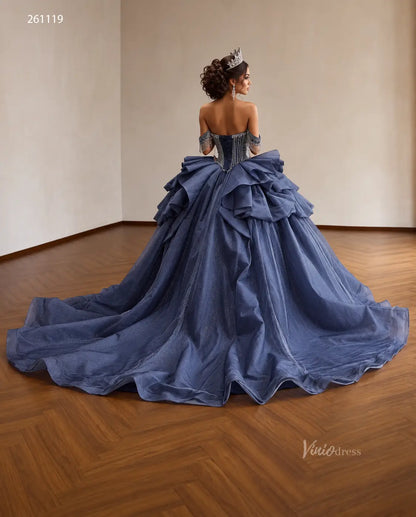 Dusty blue quinceañera dress with crystal-draped corset, off-shoulder straps, and a voluminous ruffled skirt.