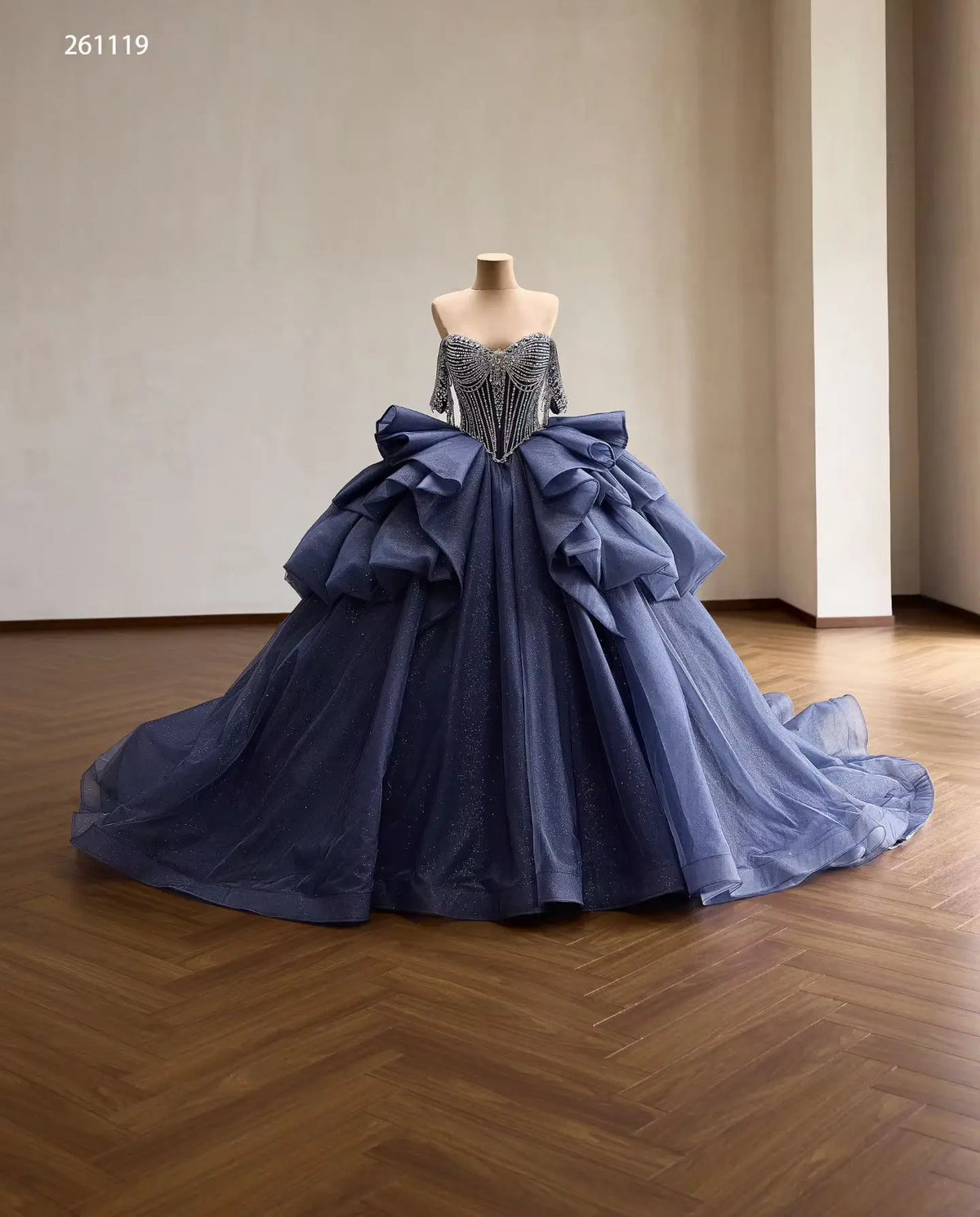 Dusty blue quinceañera dress with crystal-draped corset, off-shoulder straps, and a voluminous ruffled skirt.