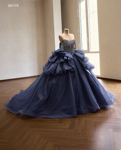 Dusty blue quinceañera dress with a crystal-draped corset, off-shoulder straps, and a voluminous ruffled skirt.