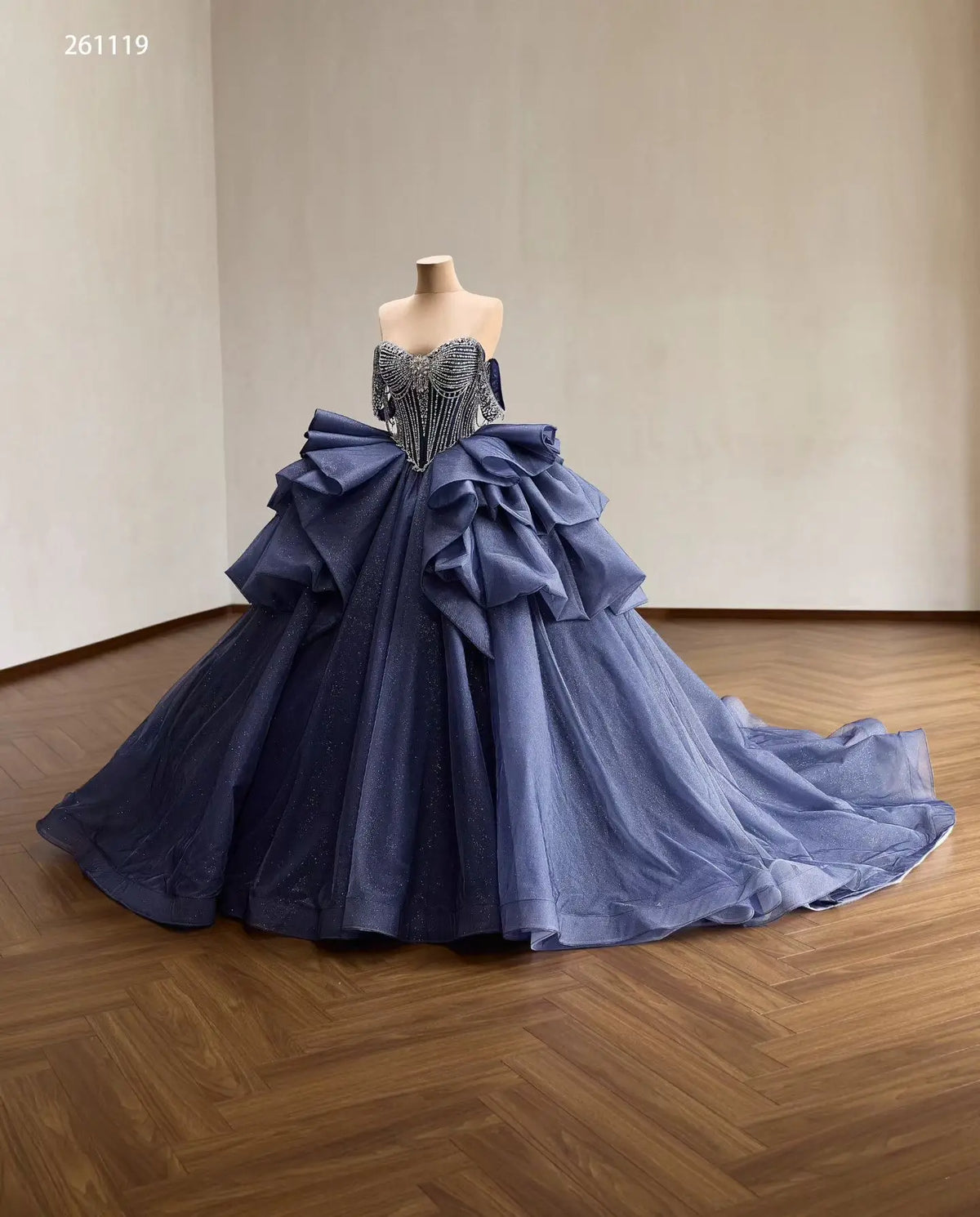 Dusty blue quinceañera dress with a crystal-draped corset, off-shoulder straps, and a voluminous ruffled skirt.