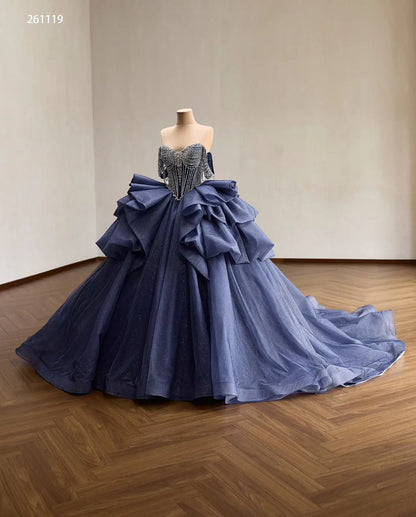 Dusty blue quinceañera dress with a crystal-draped corset, off-shoulder straps, and a voluminous ruffled skirt.