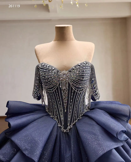 Dusty blue quinceañera dress with a crystal-draped corset, off-shoulder straps, and a dramatic ruffled skirt.