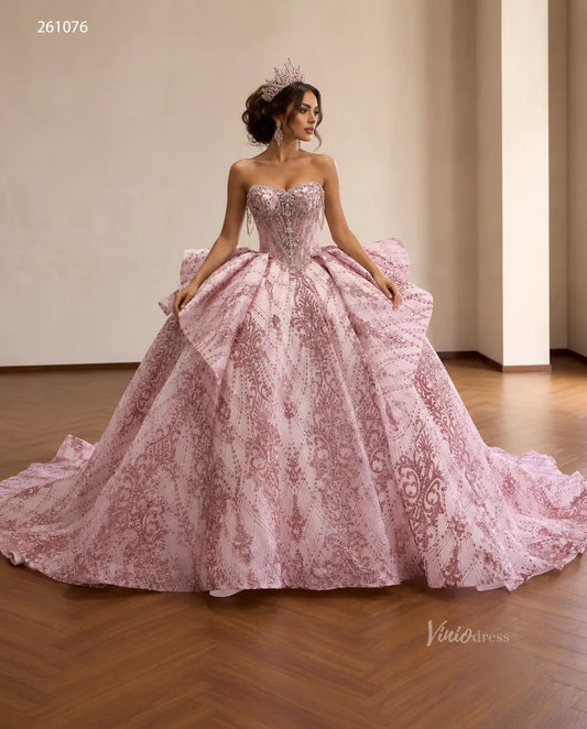 Pink quinceañera ball gown with rose-gold baroque embroidery, crystal-fringe corset bodice, and oversized sculptural bow.