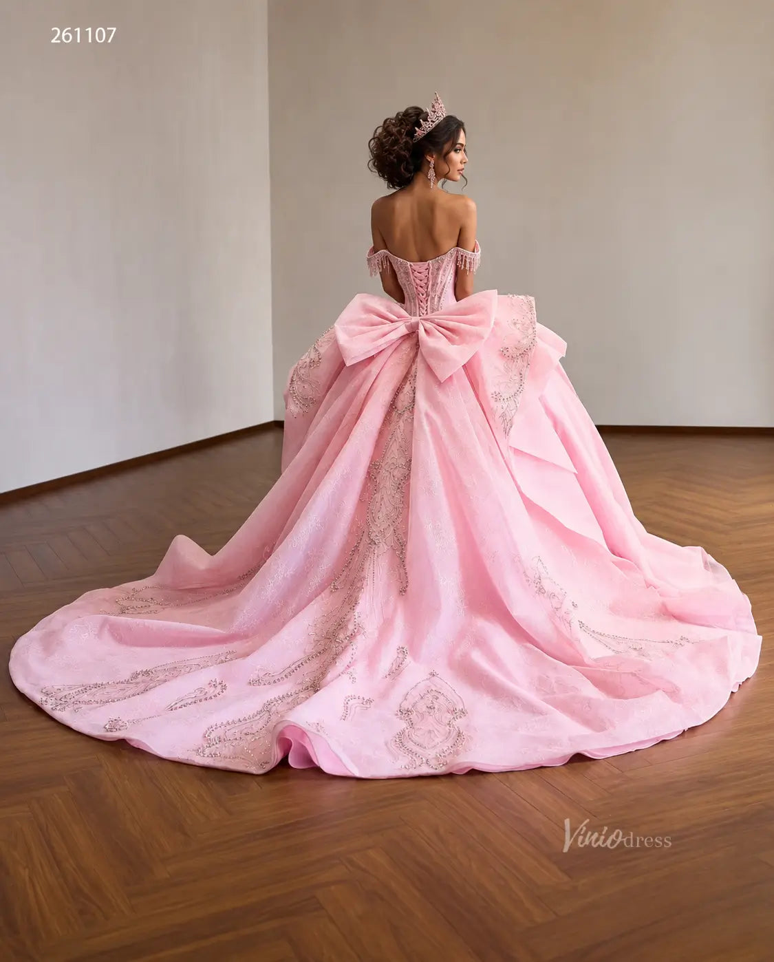 Pink quinceañera dress with crystal corset, oversized back bow, layered overskirt, and ornate silver embroidery.