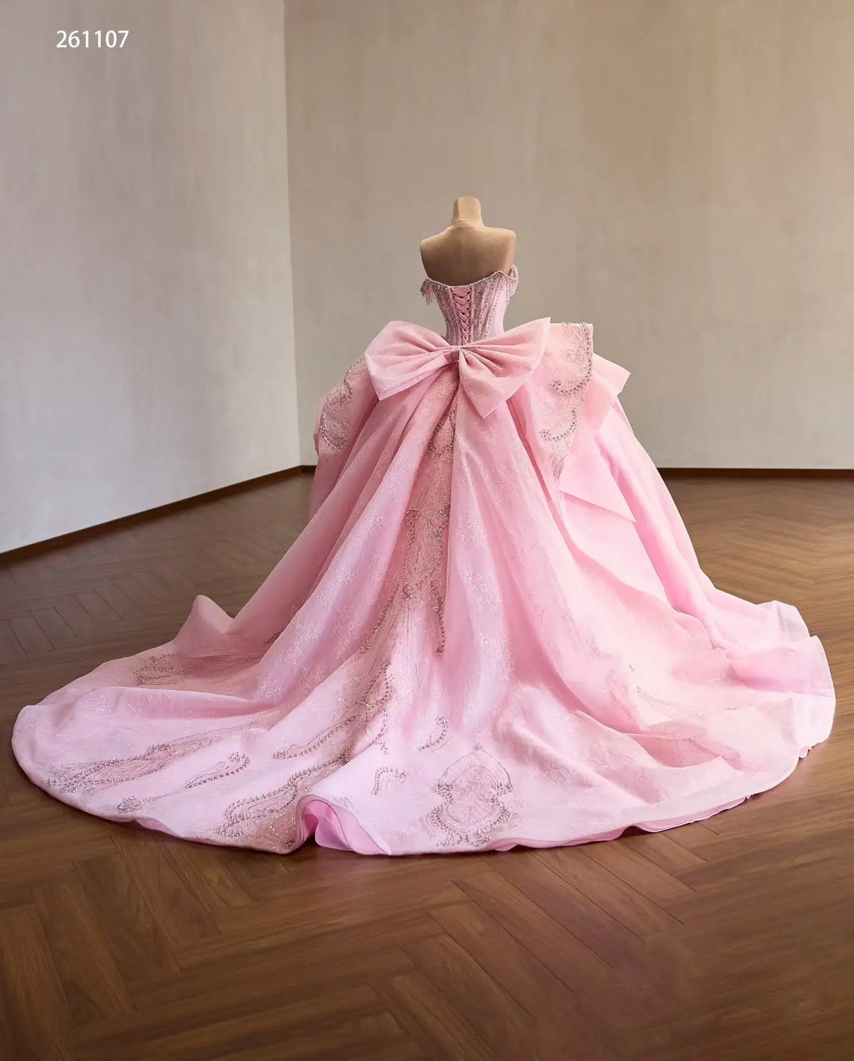 Pink quinceañera dress with a crystal corset, oversized back bow, and voluminous embroidered skirt with a long train.