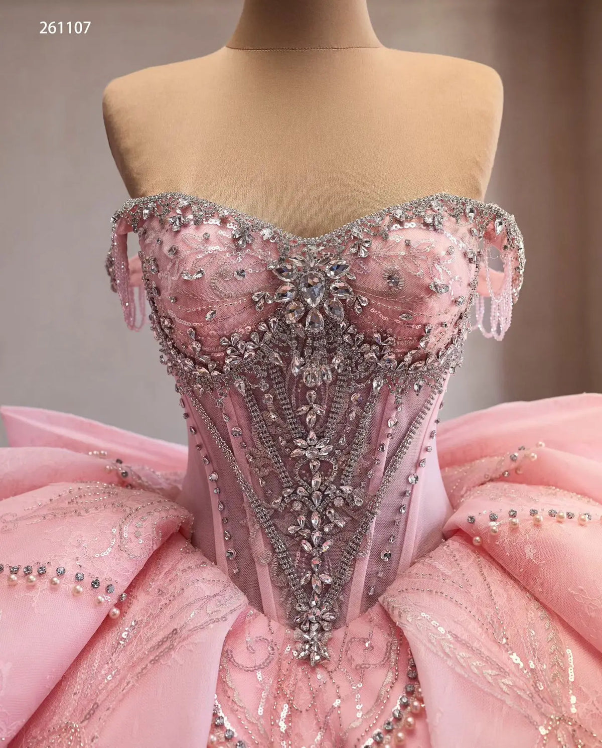Pink off-shoulder quinceañera dress featuring a crystal-beaded corset bodice, sculptural layered skirt, and fringe trim.