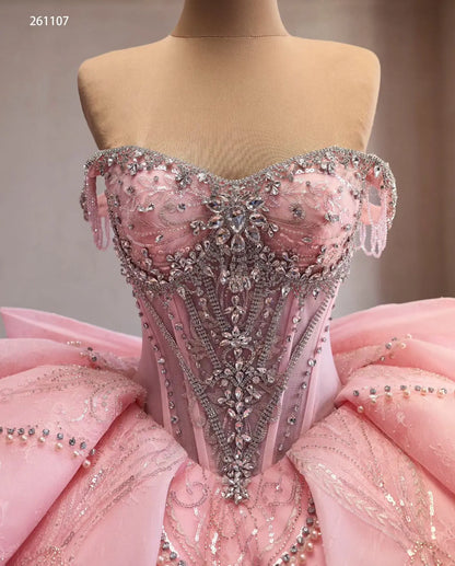 Pink off-shoulder quinceañera dress featuring a crystal-beaded corset bodice, sculptural layered skirt, and fringe trim.