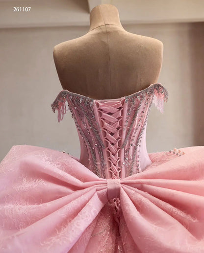 Pink quinceañera dress with crystal-beaded corset, lace-up back, and an oversized structural bow on a mannequin.