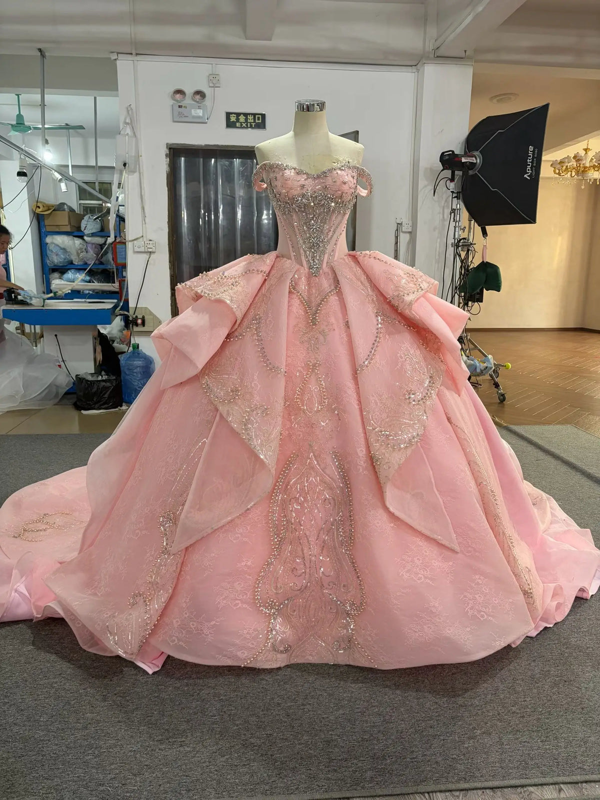 Pink off-shoulder quinceañera dress with crystal corset, sculptural layered overskirt, and ornate beaded embroidery.