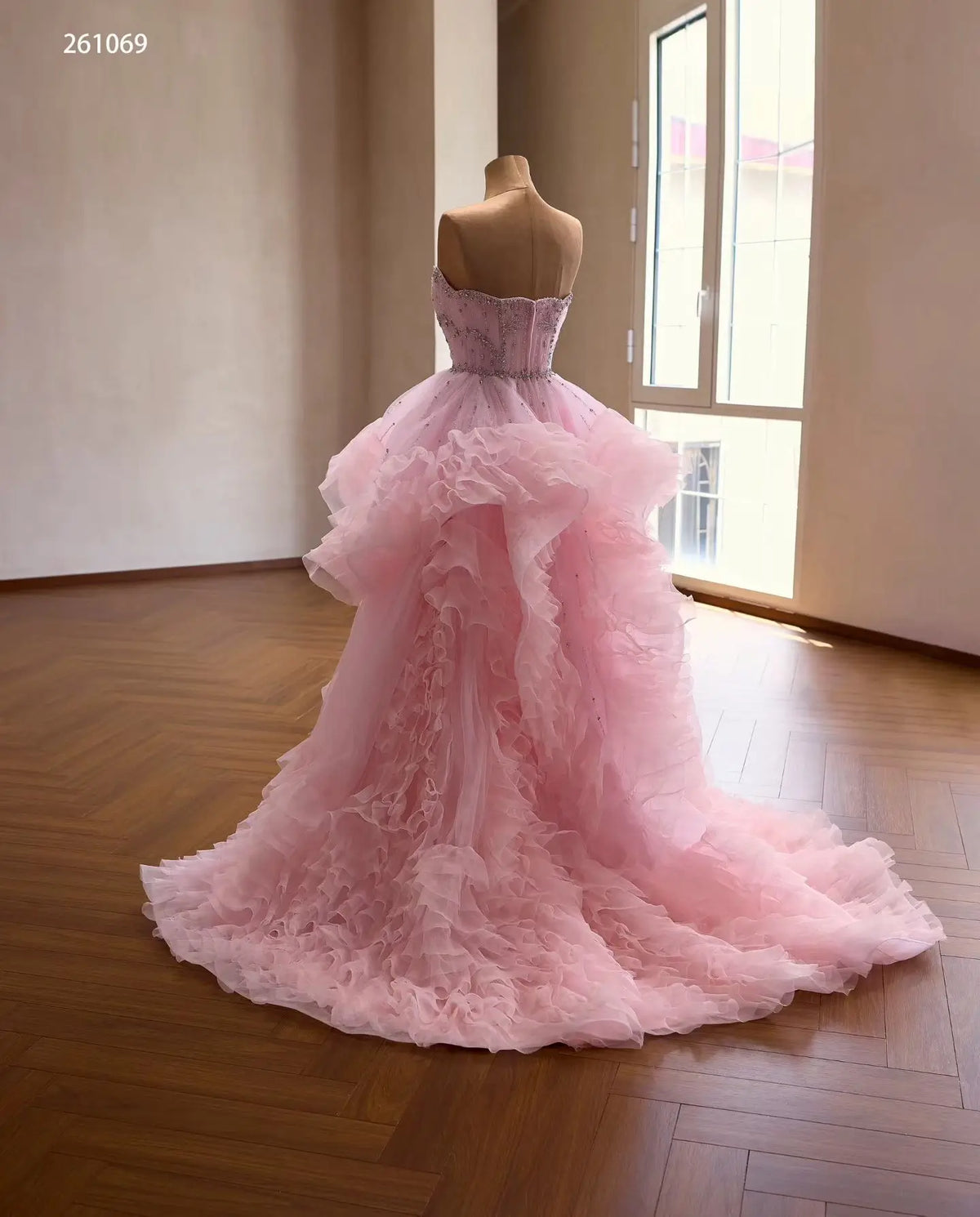 Pink tulle quinceañera ball gown with cascading waterfall ruffles and a crystal-beaded corset bodice on a mannequin.
