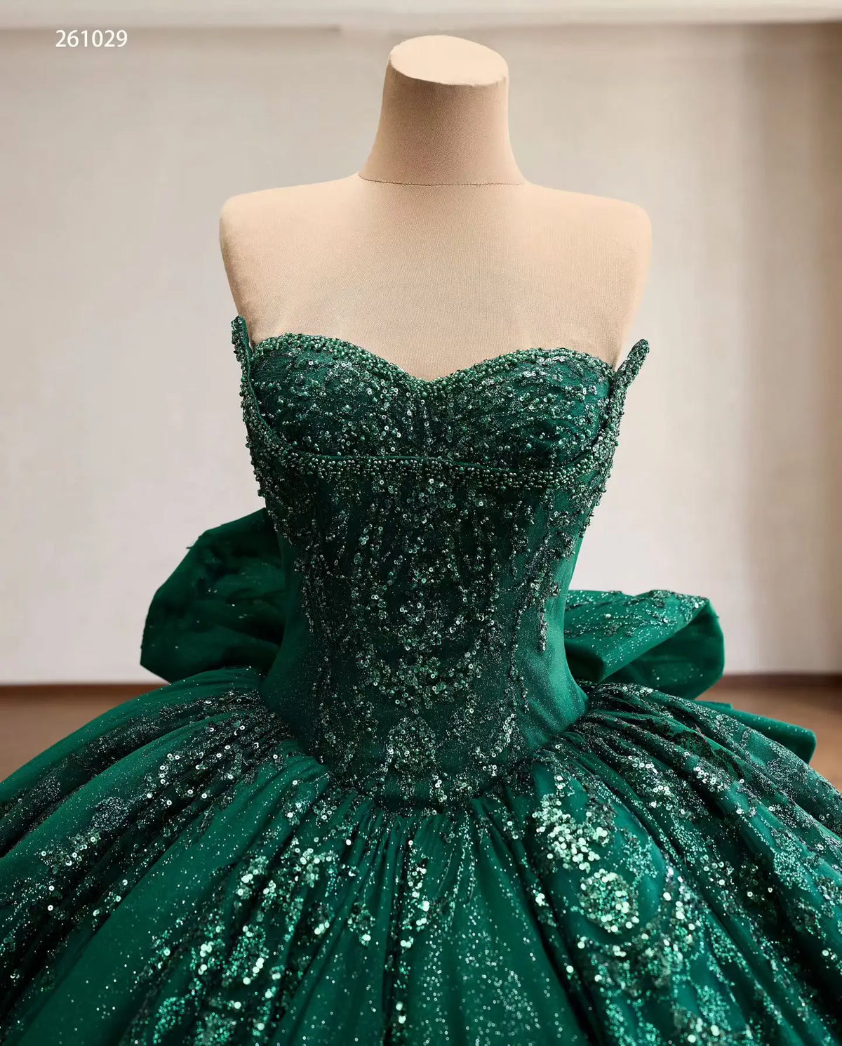Emerald green quinceañera ball gown with beaded sweetheart corset, metallic embroidery, and oversized back bow.