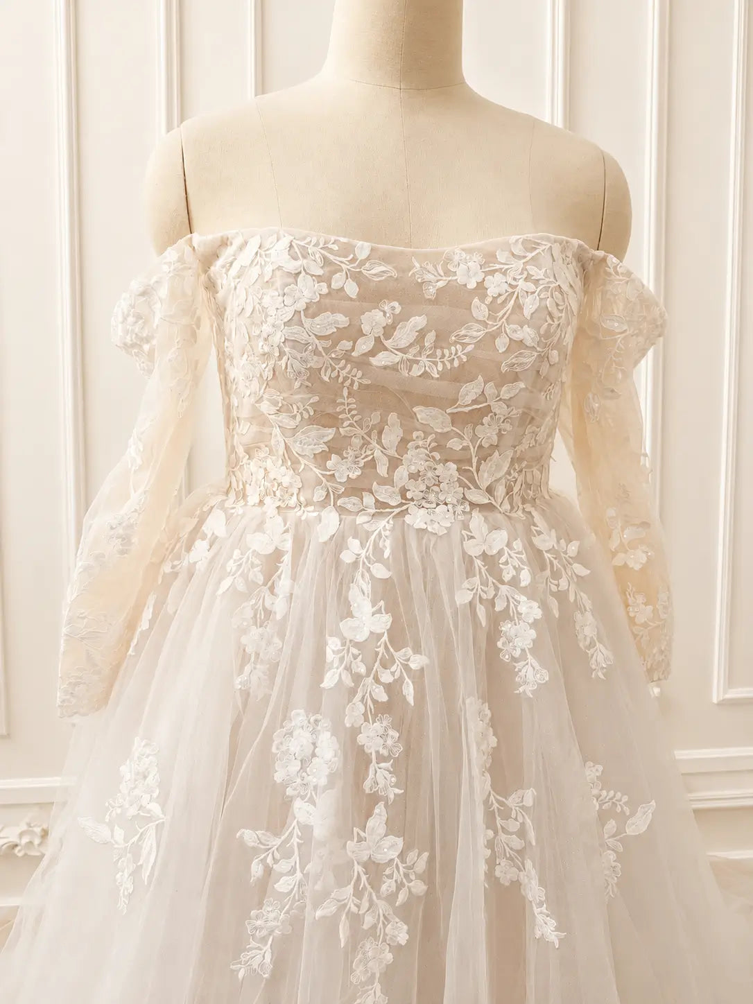 Ivory off-shoulder wedding dress with long sheer sleeves, floral lace appliqué, and a sparkling tulle A-line skirt.