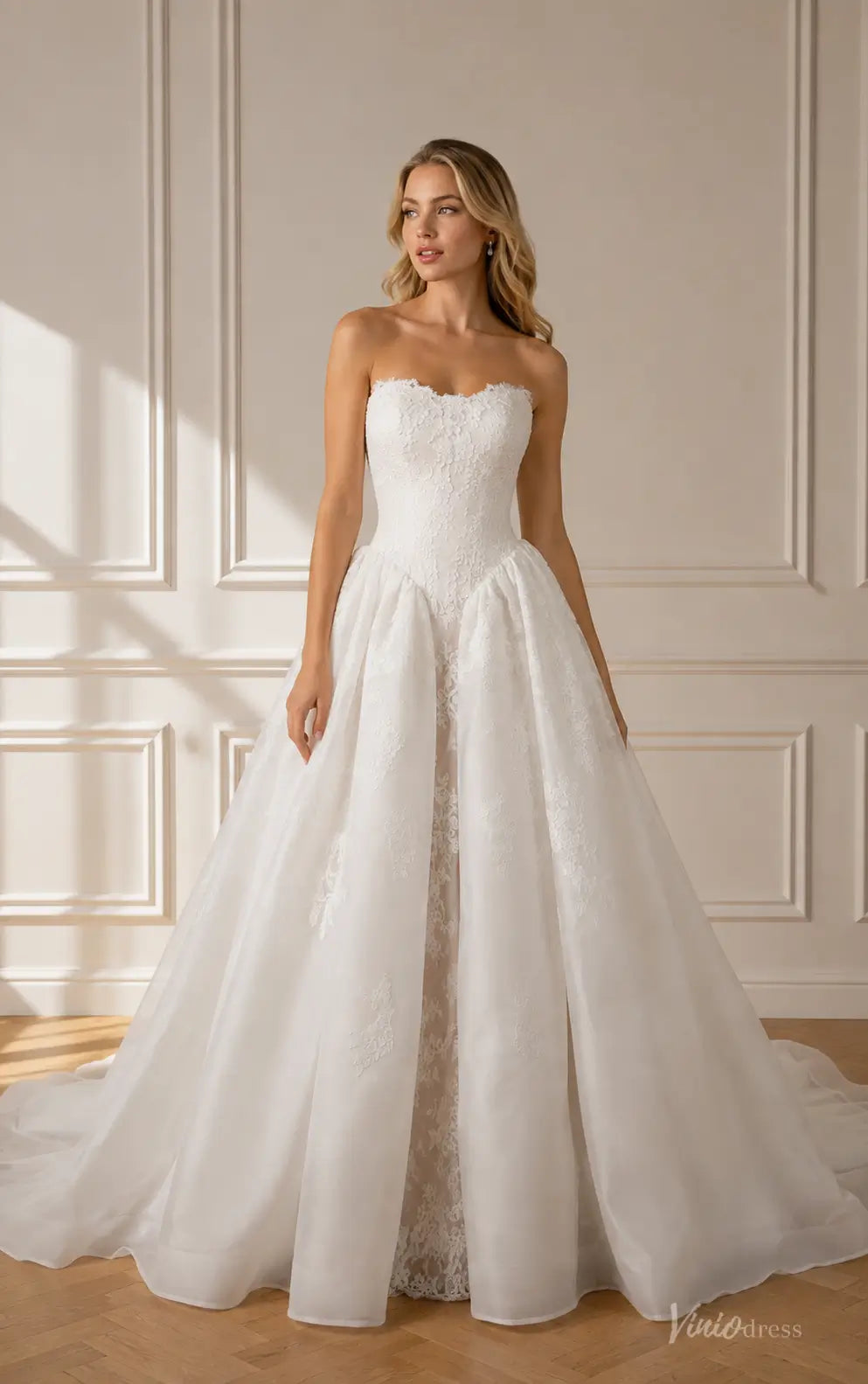 Strapless white wedding dress with a lace bodice and a voluminous organza overskirt featuring elegant floral embroidery.