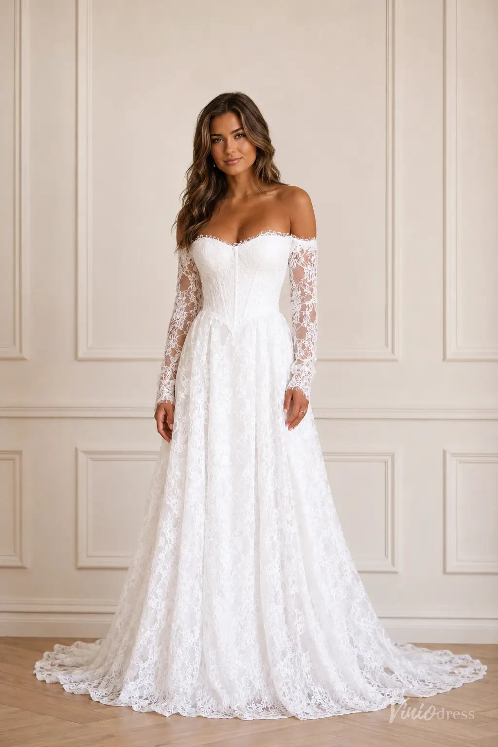White off-the-shoulder lace wedding dress with long sleeves, a corset-style bodice, and a flowing A-line skirt.