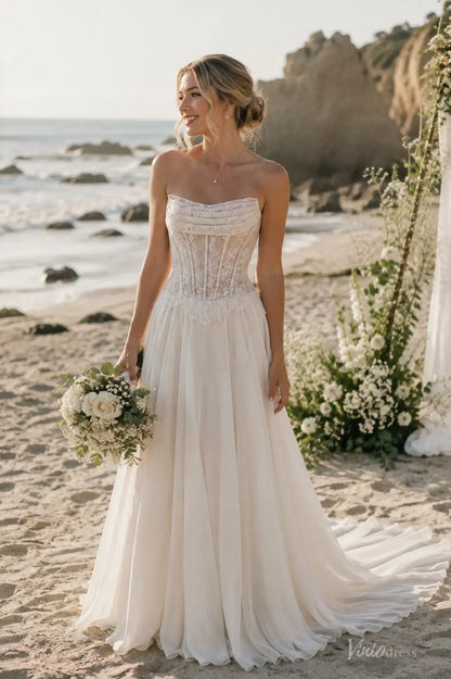 Strapless ivory beach wedding dress with a lace corset bodice and flowing chiffon skirt on a sandy shore.