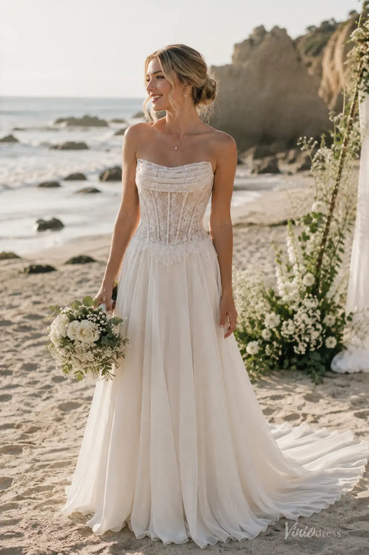Strapless ivory beach wedding dress with a lace corset bodice and flowing chiffon skirt on a sandy shore.