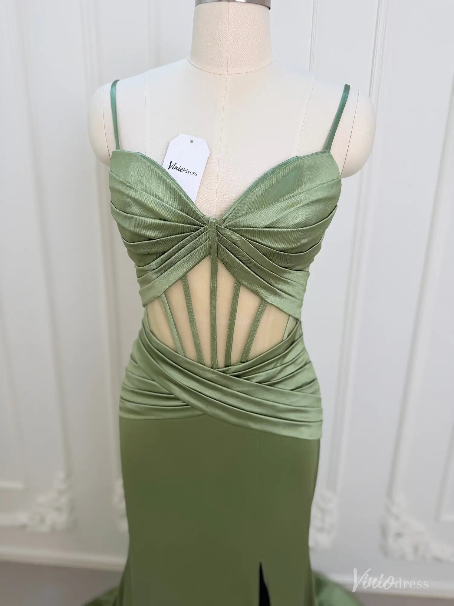 Sage green satin mermaid prom dress featuring a corset-style cutout bodice, ruched waist, and spaghetti straps.