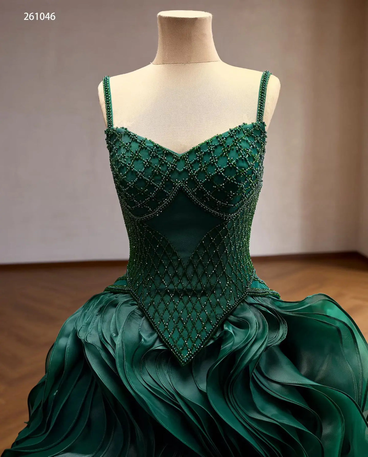 Emerald green quinceañera ball gown with a diamond-beaded basque corset, sweetheart neckline, and sculptural wave ruffle skirt.