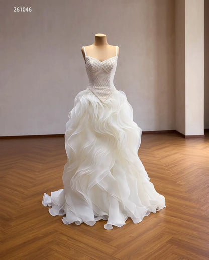 Ivory ball gown with a diamond-beaded basque corset, sweetheart neckline, and a sculptural wave ruffle skirt.