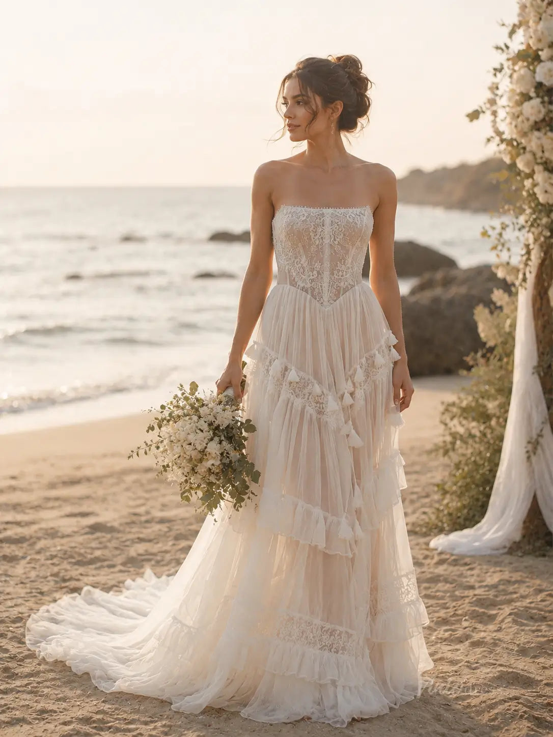 Strapless ivory wedding dress with a lace corset bodice, tiered tulle skirt, and delicate fringe trim on a beach.