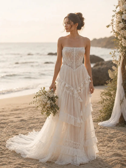 Strapless ivory wedding dress with a lace corset bodice, tiered tulle skirt, and delicate fringe trim on a beach.