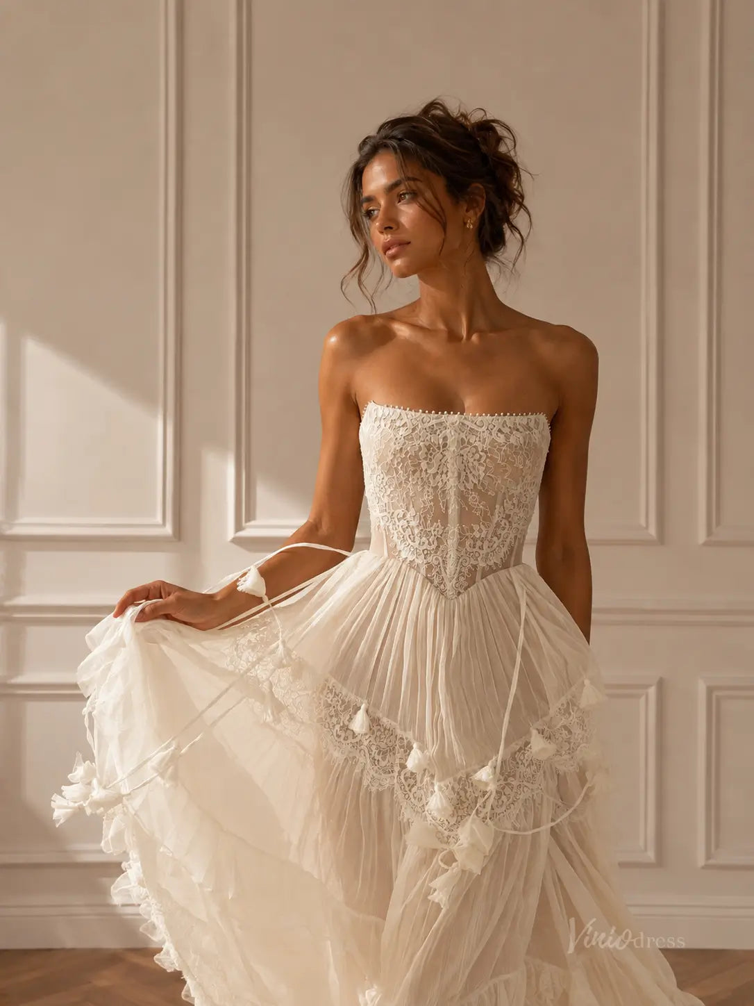 Ivory strapless corset wedding dress with intricate lace bodice, tiered pleated skirt, and delicate tassel accents.