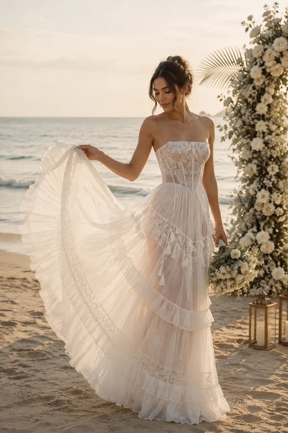 Strapless ivory wedding dress with a lace corset bodice and tiered ruffled tulle skirt on a beach at sunset.